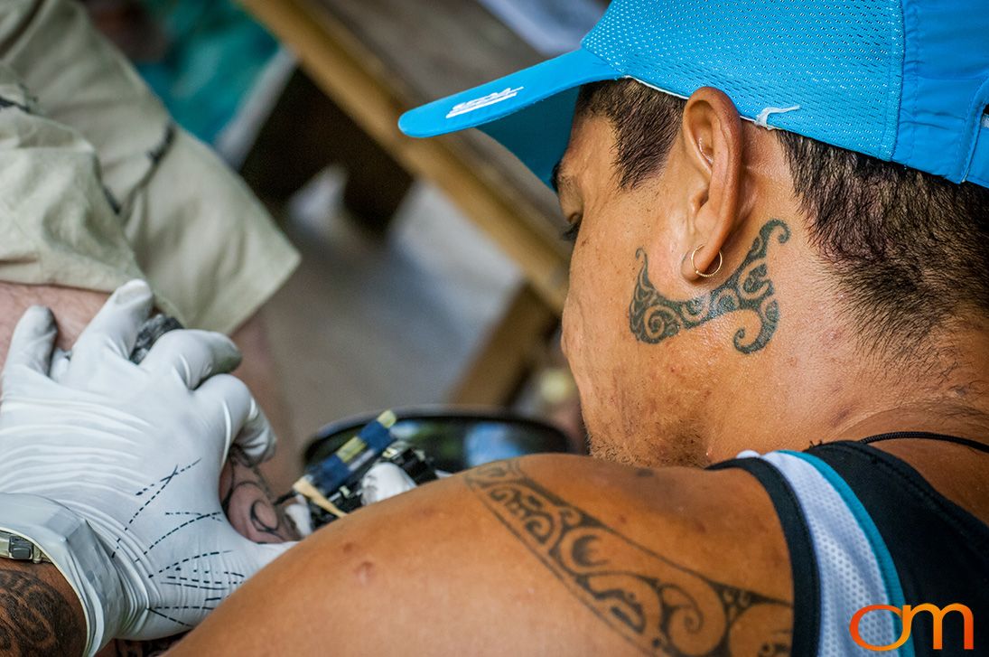 Photo of Polynesian tattoo artist applying a traditional tattoo design on a tourist's leg. Taken of Santos on the Marquesas island of Hiva Oa by Amanda Fornal in October 2006.