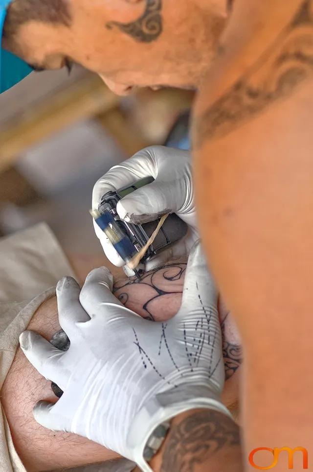 Photo of Polynesian tattoo artist applying a traditional tattoo design on a tourist's leg. Taken of Santos on the Marquesas island of Hiva Oa by Amanda Fornal in October 2006.